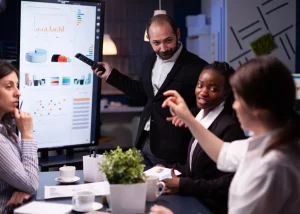 Équipe professionnelle en réunion de formation analysant des tableaux de bord de performance sur grand écran interactif.