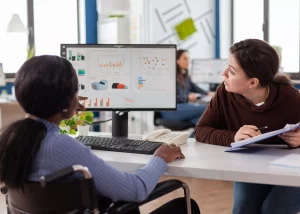 Deux collaboratrices en réunion de travail analysant des graphiques de performance et des indicateurs de gestion du changement sur un écran d'ordinateur de bureau.