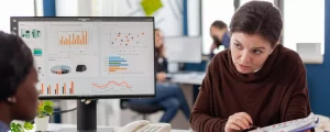 Responsable analysant un tableau de bord d'indicateurs de performance (KPI) et un rapport d'impact lors d'une réunion d'équipe au bureau.